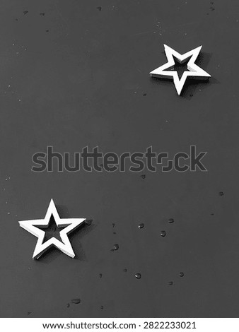 two white star-shaped objects set against a dark, textured background. The minimalist composition emphasizes the contrast between the bright stars and the shadowy surface beneath them