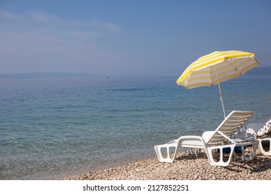 Two White Sun Loungers And Yellow Sun Umbrella Stand On The Beach