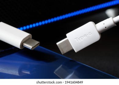 Two white USB type-c connectors next to a blue smartphone and blue LED lights. The concept of modern technologies and data transmission. Close-up. Macro. Selective focusing