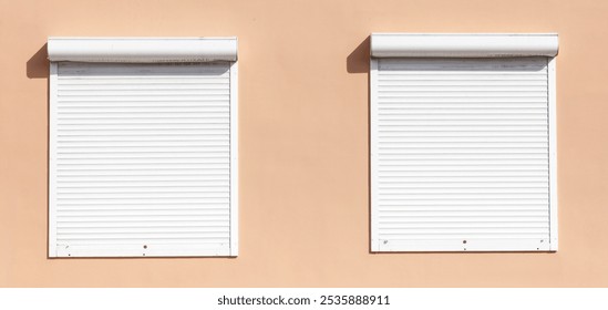 Two white windows with a white shutter on the inside. The shutter is open. The windows are on a building with a tan wall
