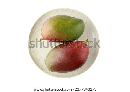 Two whole ripe mango Palmer fruits on retro plate isolated on white background.