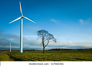 Two wind electric generators in field with alone tree. - Shutterstock ID 117065356
