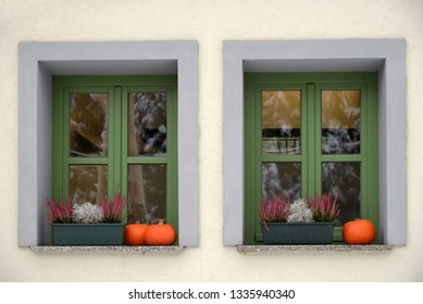 Two windows decorated with flowers in boxes and pumpkins