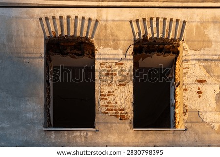 Two windows lack frames. Exposed brick peeks through cracks. Sunlight glows on weathered walls. Old building decay. Ideal for historical or urban stories. Capture timeless architectural wear
