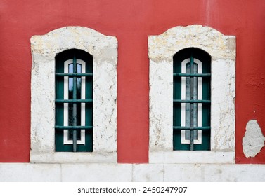 
two windows on a red wall. The windows are stylish with white frames on the wall. Exterior facade of a red historic apartment house in Lisbon, Portugal. Urban background