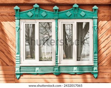 Two windows with shabby carved wooden architraves emerald color on plank facade of 19th century wood house . Nizhny Novgorod region, Russia. Architecture concept