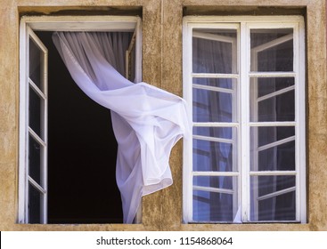 Two windows viewed from outside, one is closed and another is open with slight curtain caught on wall