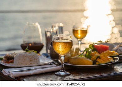 Two wine glasses and food on wooden table near sea on the tropical beach during sunset. The concept of a romantic dinner - Powered by Shutterstock