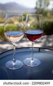 Two Wine Glasses Next To Each Other Filled With White And Red Wine Against A Wine Farm Backdrop