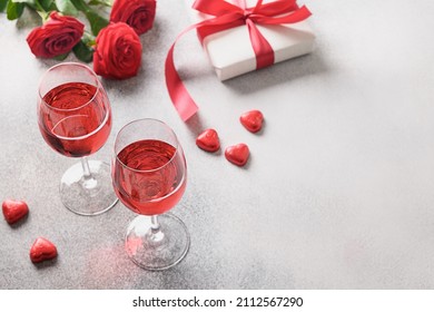 Two wine glasses with red wine for romantic dating or Valentine's day dinner with red rose flowers on gray background. Copy space. Close up.