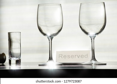  Two wine glasses and a shotglass on a top of unoccupiesd table with a sign "reserved" that indicates the reservation has ben made