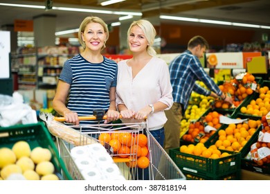 Two woman choosing seasonal fruits in grocery section of supermarket