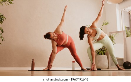 Two woman doing yoga at fitness studio. Fitness females doing Triangle yoga Pose, Trikonasana at gym.
