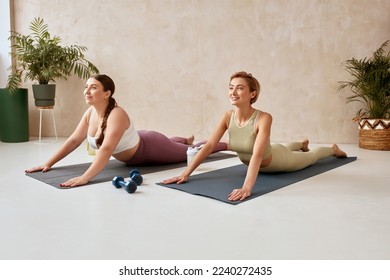 Two Woman Exercising Yoga. Female Friends Doing Cobra Pose Together At Home. Attractive Girls In Sportswear Using Mat Spending Free Leisure Time Exercise For Health Care And Wellness  - Powered by Shutterstock