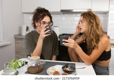 Two Woman Friends Breakfast In The Kitchen And Having Fun, Talking And Laughing, Sitting At The Dining Table At Home.