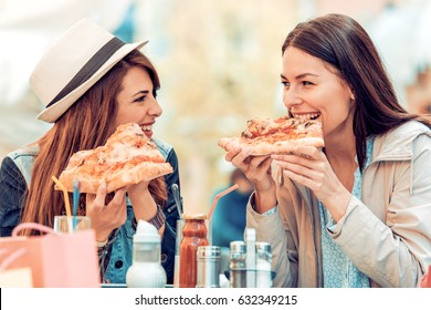 Two woman having fun in cafe,eating pizza together.