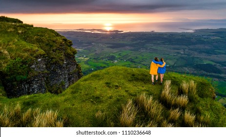 Two Woman Hiking In The Mountains With A Rain Jacket One Yellow And The Other Blue On A Cloudy Summer Day In Ireland. Hiking In The Mountains.