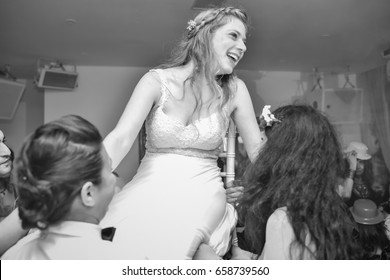 two woman lifting the bride with the chair into the air on the dance floor
