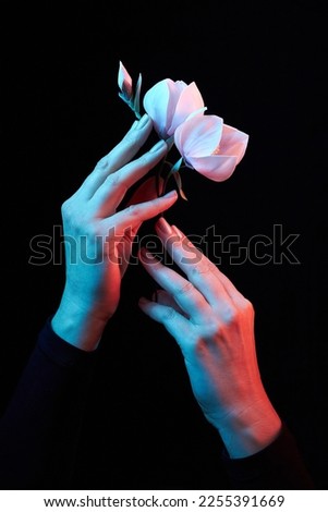 Two woman's hands holding pink blooming artificial magnolia flower from foamiran on dark background. Close up and isolated