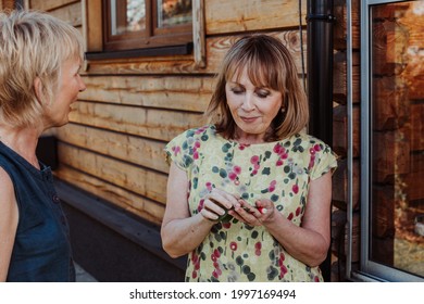 Two Women 55-59 Years Communicate In Nature On The Background Of Wooden House