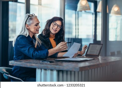 Two women analyzing documents while sitting on a table in office. Woman executives at work in office discussing some paperwork.