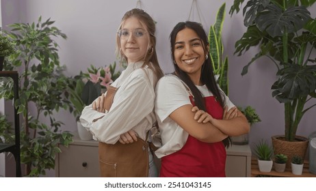 Two women, arms crossed, standing together amidst potted plants, evoke teamwork in a flower shop setting. - Powered by Shutterstock