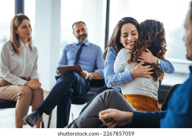 The two women are attending a group therapy session. They are showing support and kindness. Portrait of female psychologist embracing young woman during therapy session in support group - Powered by Shutterstock