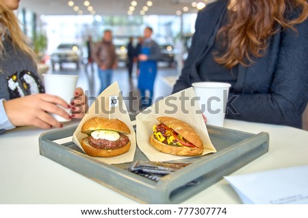 two women chatting during lunch. on a table delicious burger with fried meat cutlet, hot-dog, placed in wooden tray.
