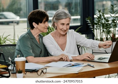 Two women collaborate on a project while reviewing information on a laptop. - Powered by Shutterstock