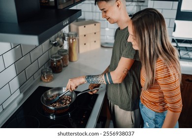 Two women are cooking together in their modern kitchen, stirring ingredients in a pan on the stovetop, enjoying their time together and creating a delicious meal - Powered by Shutterstock