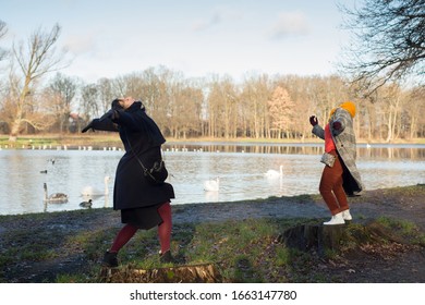 Two women dancing in a park by the lake with swans