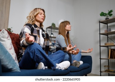 Two Women Of Different Ages Meditate Sitting In The Lotus Position On The Couch