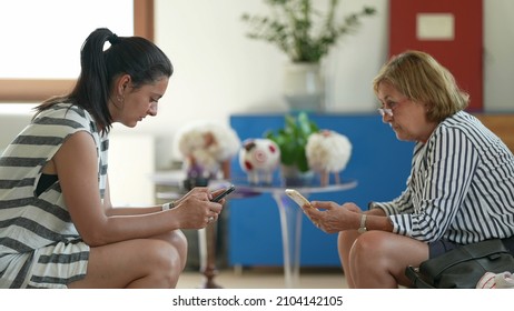 Two Women From Different Generations Looking At Smartphone Devices Separately