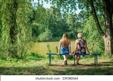 Two women of different generations sitting on a bench near a pond in the summer. Mother and daughter hugging. Grandmother and granddaughter.