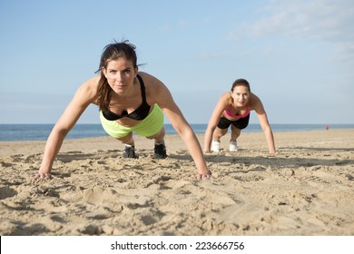 Two women doing pushups on a beach during an intense workout - Powered by Shutterstock