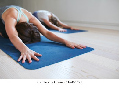 Two women doing stretching workout on fitness mat. Females performing yoga on exercise mat at gym. Child Pose, Balasana. - Powered by Shutterstock