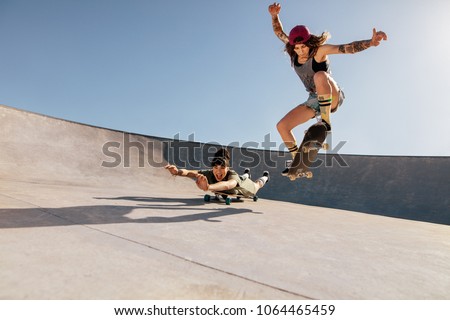 Two women doing stunts on skateboards at skate park. Female friends practising skateboarding outdoors.
