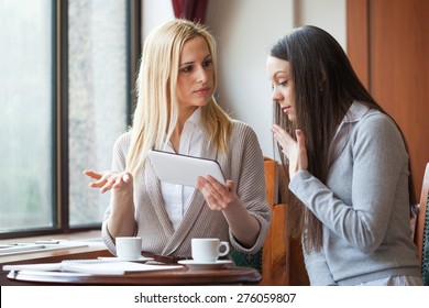 Two Women Drinking Coffee And Using Digital Tablet In Cafe