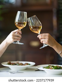 Two women are drinking wine. Two glasses of white wine in female hands. Lunch at restaurant. Wine and vegetable salad. Italian food. Italian restaurant. Soft focus.