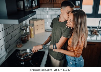 Two women are embracing and kissing while cooking a meal together in their modern kitchen, demonstrating love, togetherness, and shared domesticity - Powered by Shutterstock