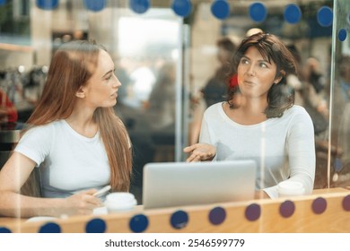 Two women engaged in a lively conversation over coffee at a cafe during the afternoon - Powered by Shutterstock