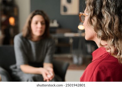 Two women engaging in a one-on-one counseling session in a cozy, well-lit room, one expressing herself while the other listens attentively. Background elements include furniture and decor - Powered by Shutterstock