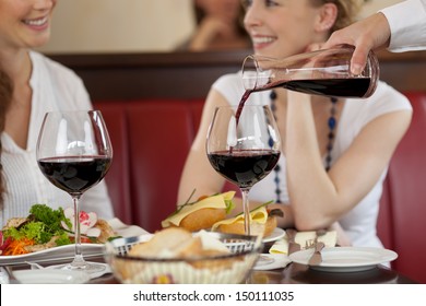 Two women enjoying red wine sitting eating a meal in a restaurant and chatting while the waiter replenishes their glasses - Powered by Shutterstock