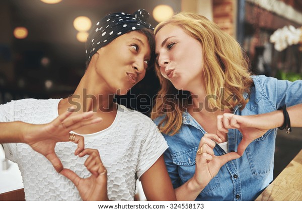 Two women\
ethnic friends kissing each other for\
fun