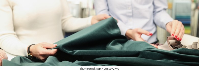 Two Women Examine Fabric Of Green Emerald Color. Custom Tailoring Concept