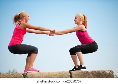 Two Women Exercise On Beach Doing Squats