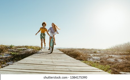 Two women friends with a bicycle on the seaside boardwalk. Woman riding the bike with her friends holding from the back and running. - Powered by Shutterstock