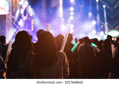 Two Women Friends Crowd Concert Stage Lights And People Fan Audience Silhouette Raising Hands Glow Stick In The Music Festival Rear View With Spotlight Glowing Effect