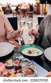 Two Women Friends Eating Fresh Oysters And Drinking Chilled Prosecco Wine On The Summer Sunset In Restaurant. Seafood Delicacies