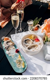 Two Women Friends Eating Fresh Oysters And Drinking Chilled Prosecco Wine On The Summer Sunset In Restaurant. Seafood Delicacies